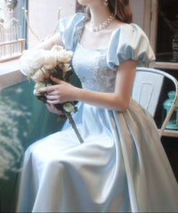 Woman in a light blue dress holding flowers indoors