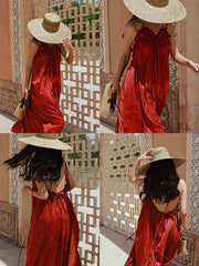 Woman in a red dress and straw hat posing against a decorative wall.