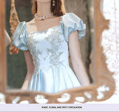 Woman in a light blue dress with floral embroidery standing in front of a mirror.