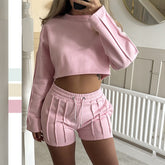 Person wearing a pink sweatshirt and shorts set in a neutral-colored room.