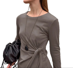 Woman wearing a gray long-sleeve dress holding a black handbag on a white background