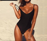 A woman wearing a black backless monokini swimsuit, posing on the beach with a brand logo 'Avenues Style' visible in the top right corner.