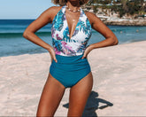A woman posing on the beach wearing a floral print monokini swimsuit with a deep v-neck and tie at the neck.