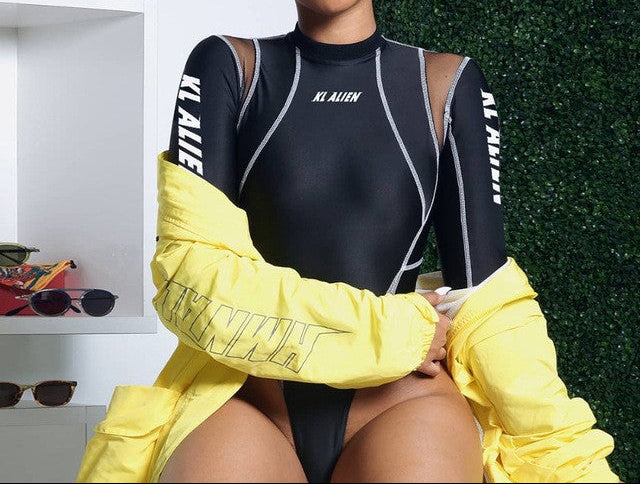 A woman wearing a black full sleeve casual romper with yellow accents and lettering, sitting in a store with sunglasses and accessories in the background.