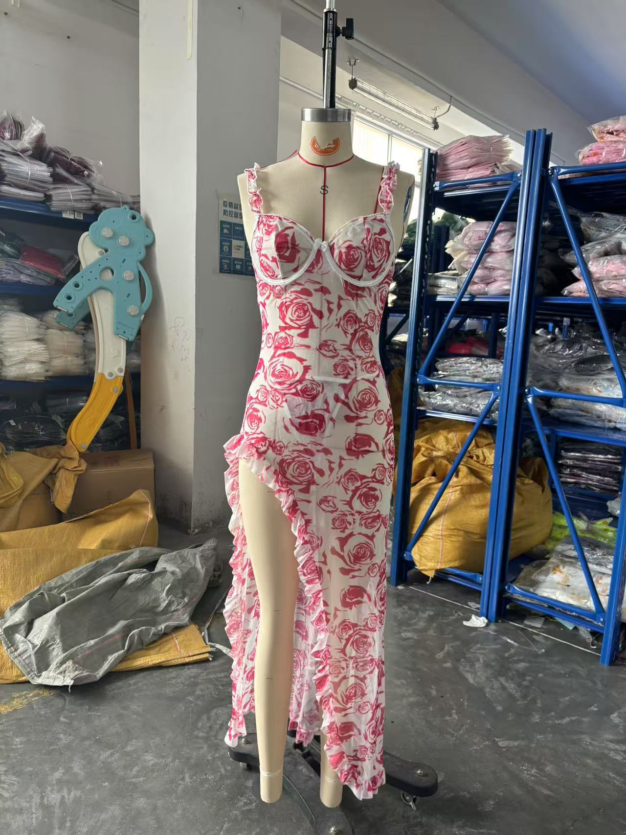 Mannequin wearing a red floral dress in a storage room with shelves and materials.