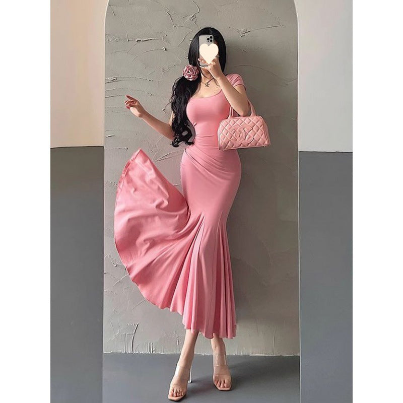 Woman in a pink dress taking a mirror selfie against a plain wall.