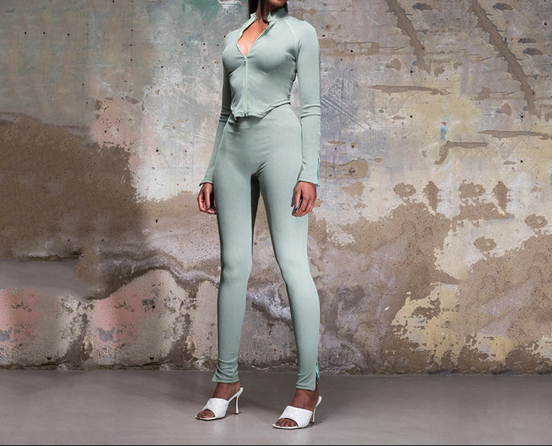 Woman in a light green outfit standing against a textured wall.