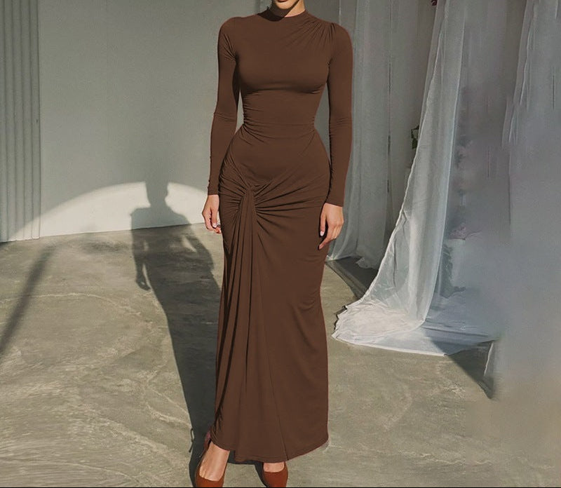 Woman wearing a brown dress standing in a softly lit room with curtains.