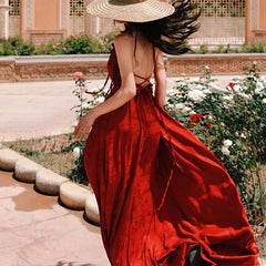 Woman in a red dress with a wide-brimmed hat walking through a garden.