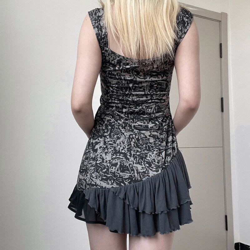 Person wearing a black and gray patterned dress with ruffled hem against a plain background