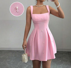 Woman wearing a pink dress with pearl details, holding a matching handbag.