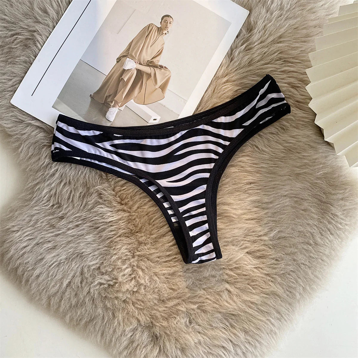 Black and white striped G-string with black trim arranged on a soft beige surface beside a magazine.