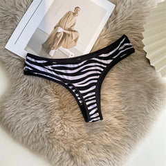 Black and white striped G-string with black trim arranged on a soft beige surface beside a magazine.