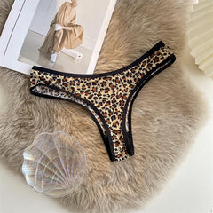 Leopard-print G-string with black trim laid flat on a textured beige surface beside a magazine and shell.