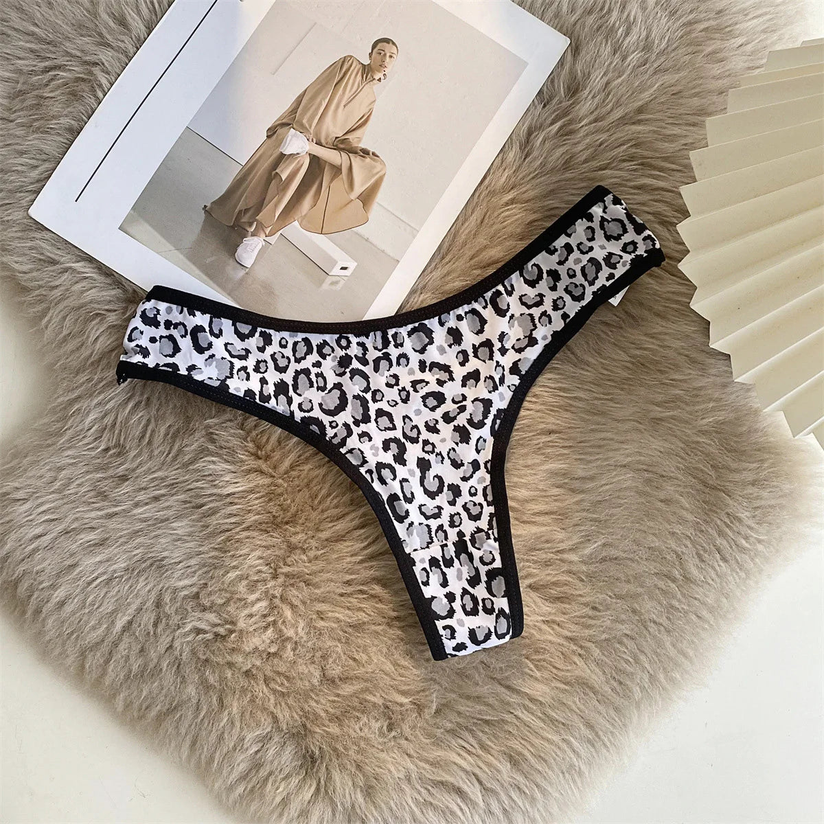 White and black leopard-print G-string with black trim displayed flat on a beige textured surface.