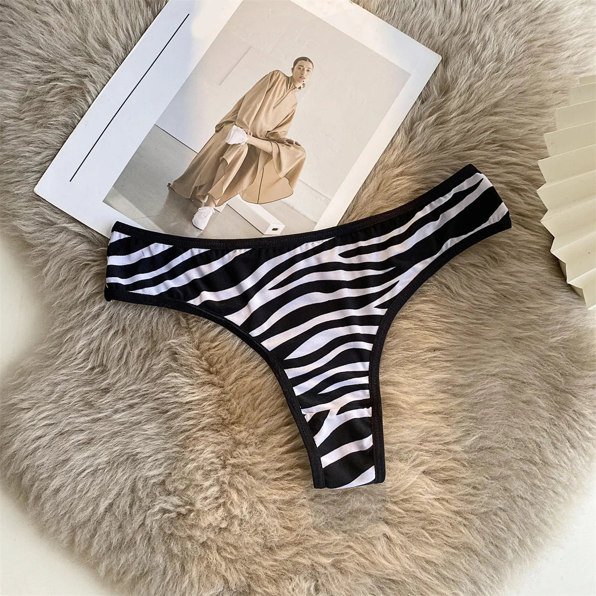 Black and white striped G-string with black trim arranged flat on a soft beige surface beside a magazine.