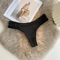 Black thong on a fluffy beige surface with a magazine in the background