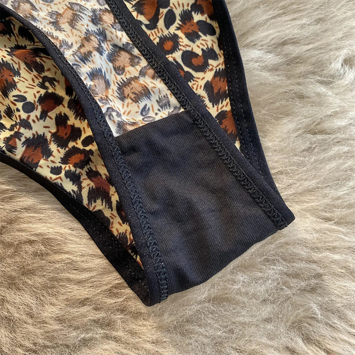 Close-up of leopard-print G-string fabric with black trim and gusset on a soft neutral surface.