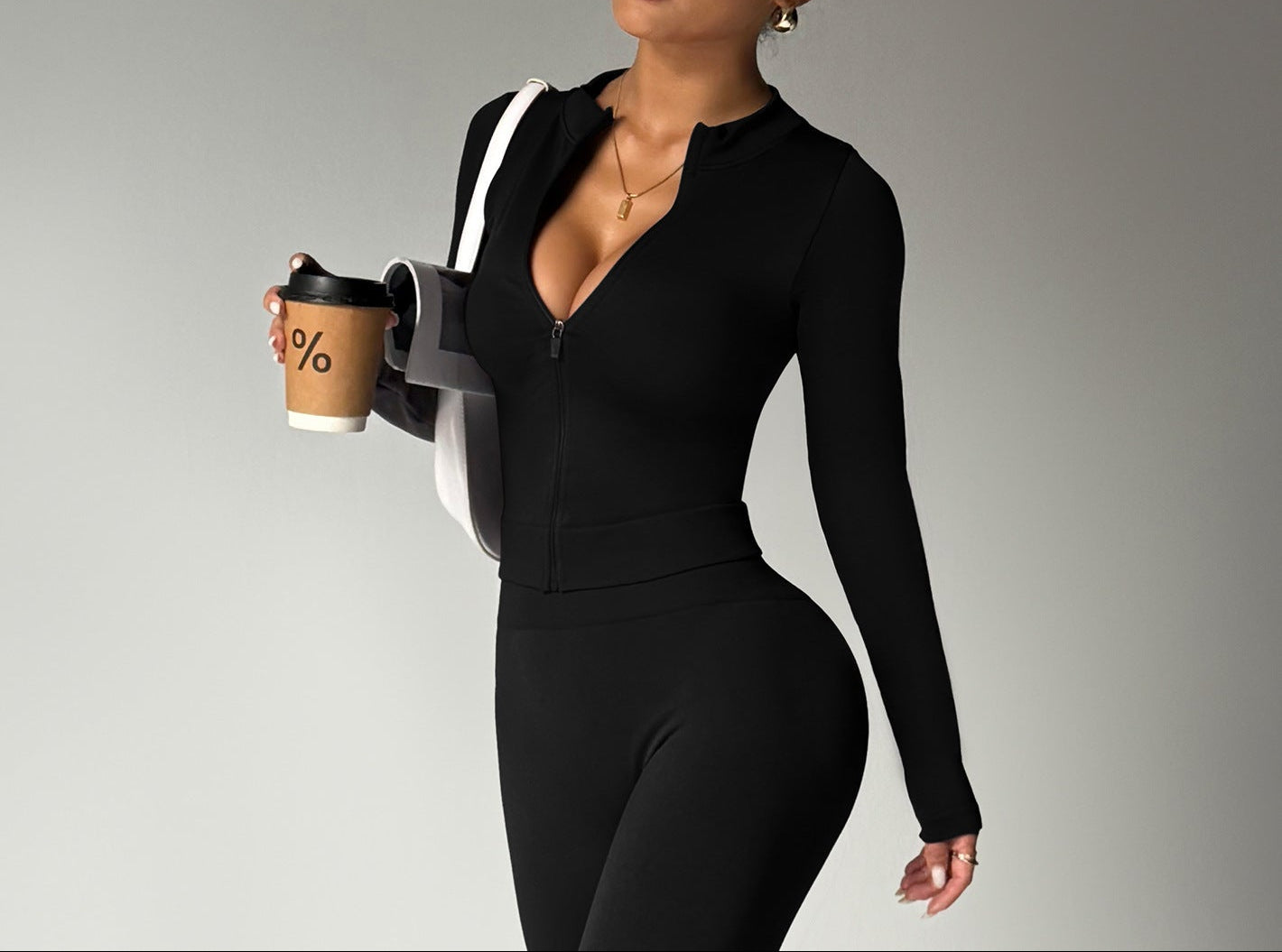 Woman in a black outfit holding a coffee cup against a gray background
