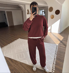 Person wearing a burgundy tracksuit taking a mirror selfie in a modern interior setting.