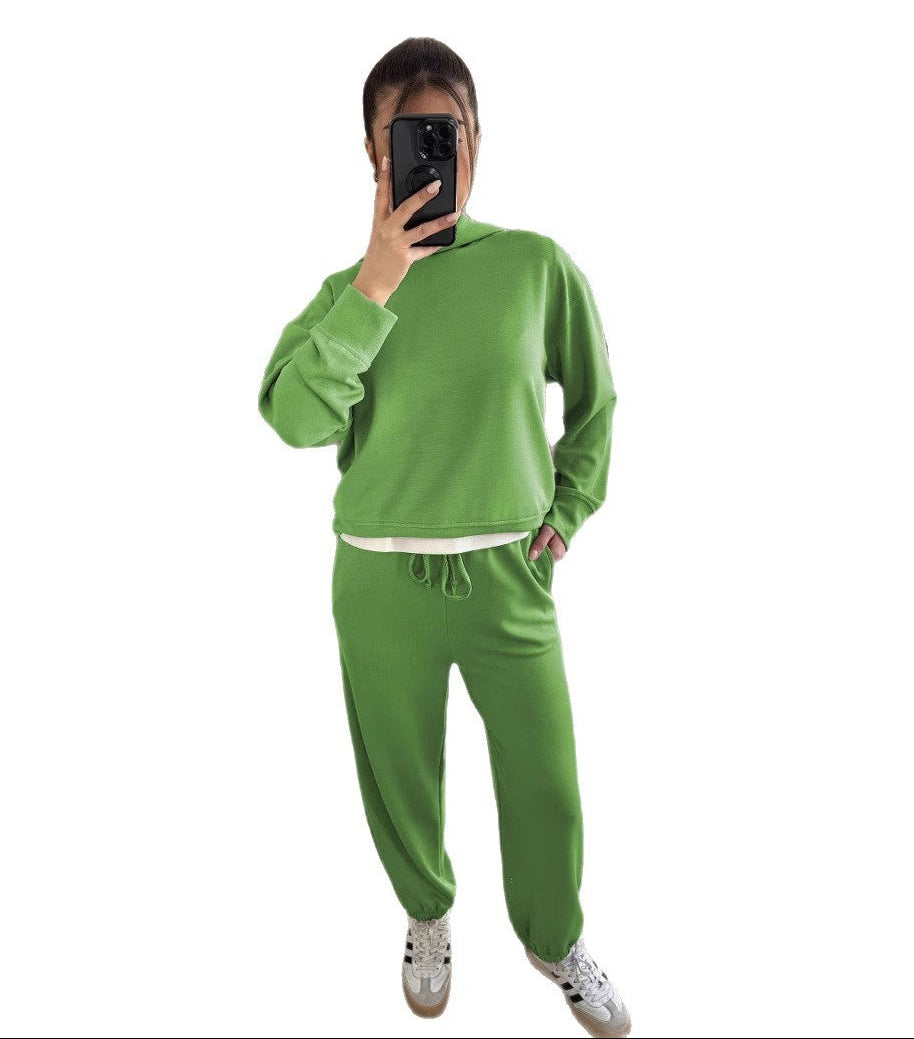 Person wearing a green tracksuit taking a mirror selfie on a white background