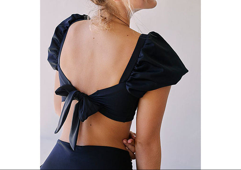 Woman wearing a black open-back top with puffed sleeves against a white background