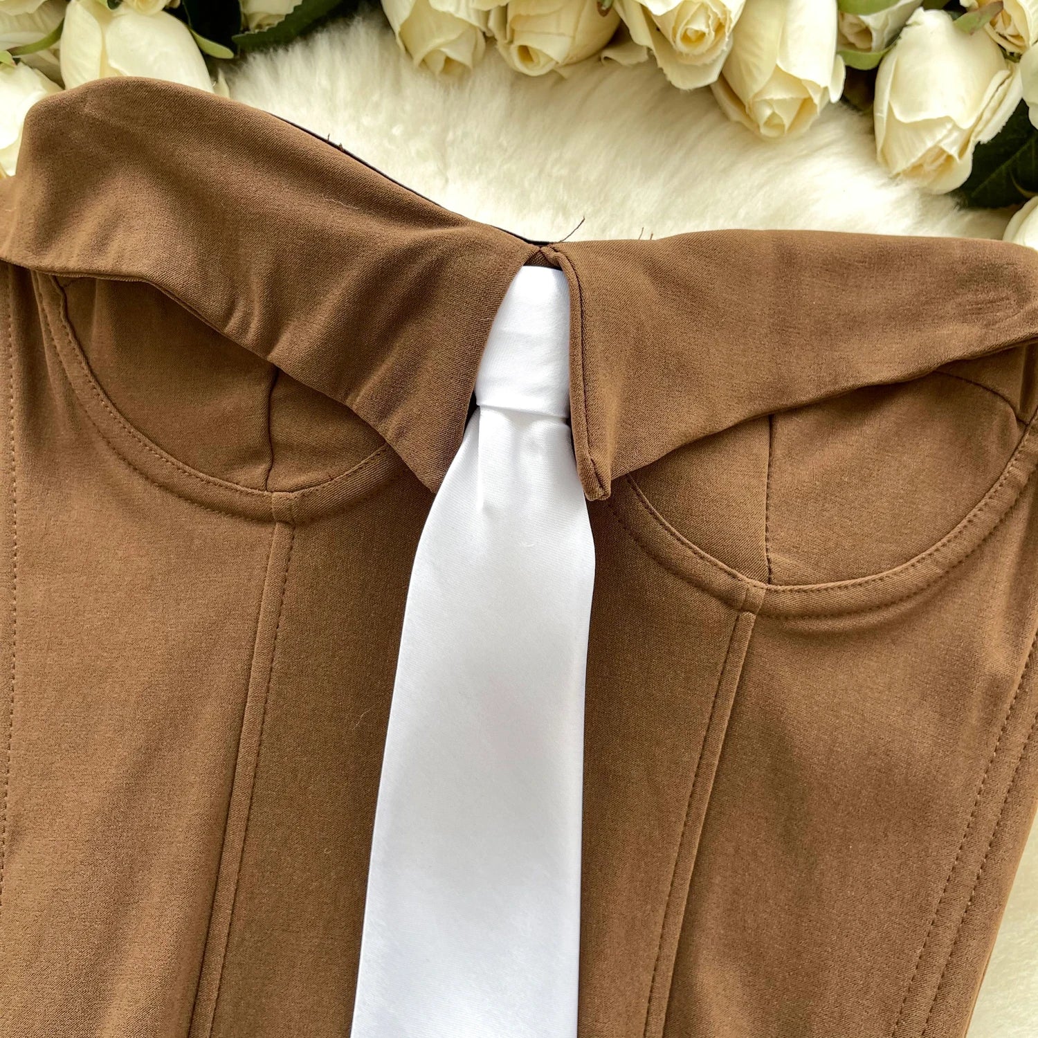 Brown garment with a white ribbon against a floral background