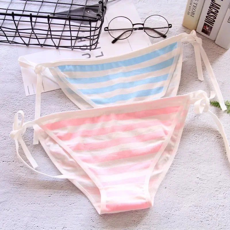Two striped bikini bottoms on a textured surface with glasses and books in the background.