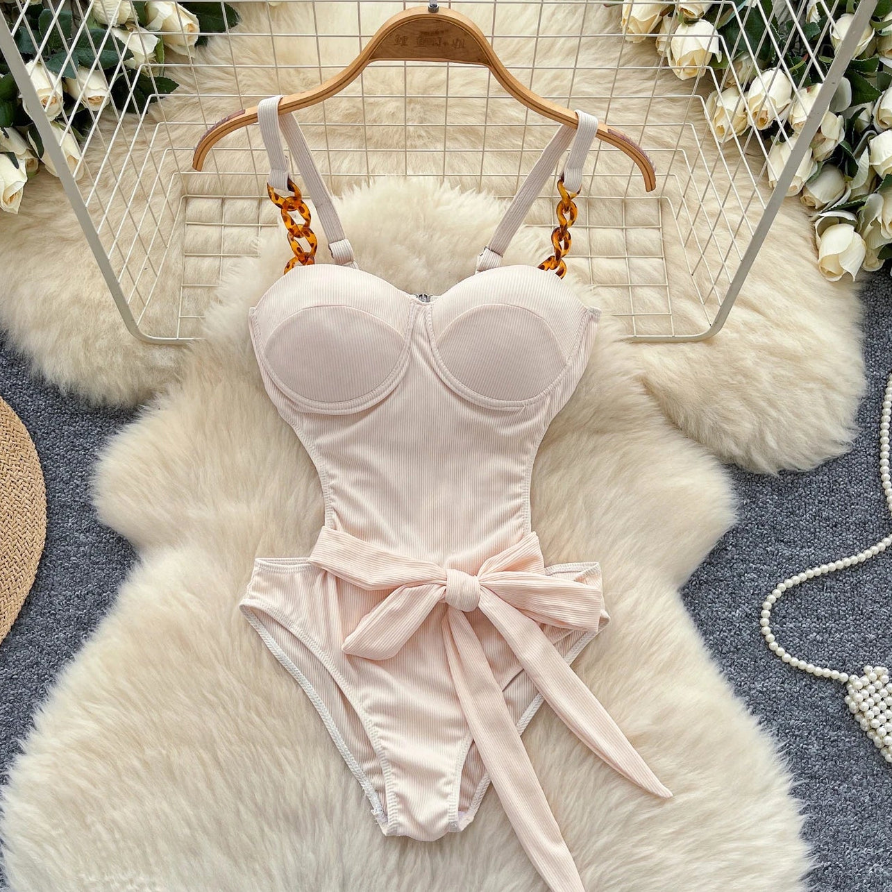 Pink swimsuit with a bow on a white fur rug with floral decorations.
