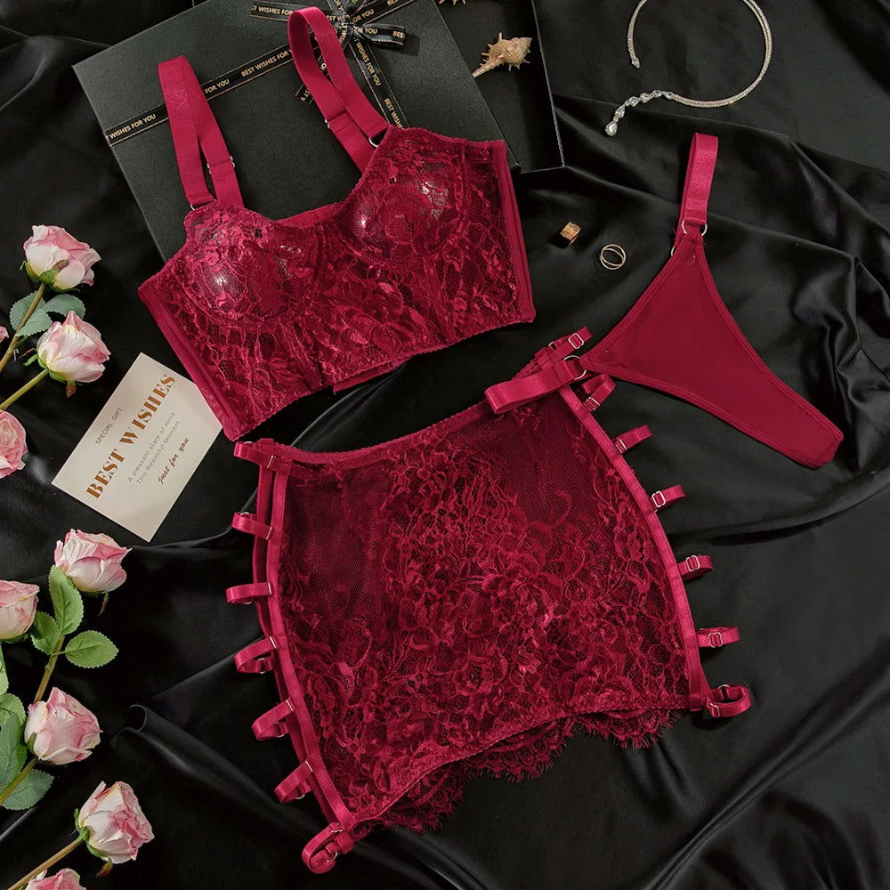 Red lace lingerie set on a black satin surface with flowers and a card.