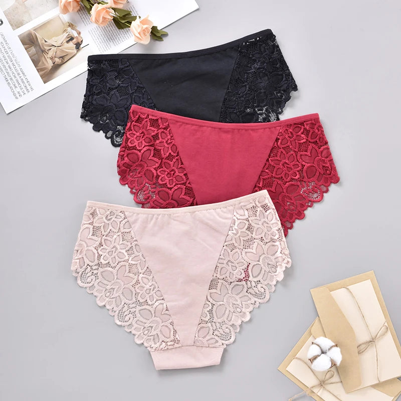 Three pairs of lace-trimmed panties in black, red, and beige on a gray surface.