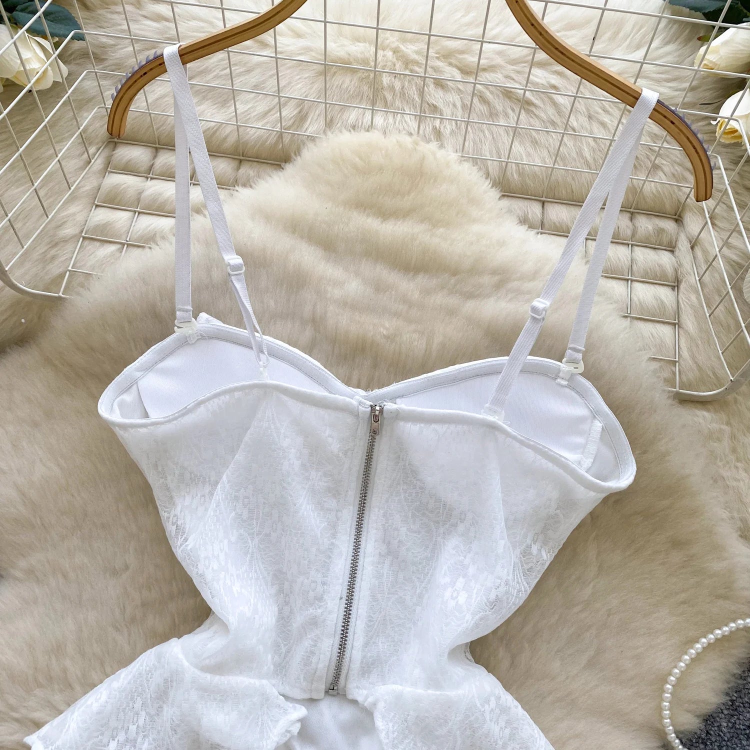 White lace dress with a zipper on a hanger against a textured beige background