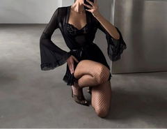 Person in a black outfit with sheer sleeves and fishnet stockings taking a mirror selfie.