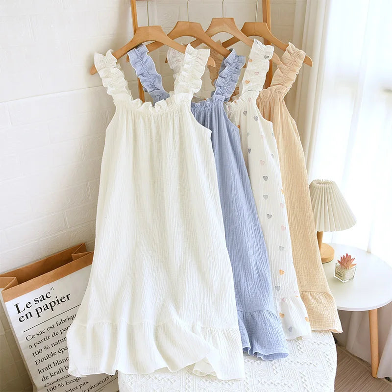 Three dresses in white, blue, and beige hanging on wooden hangers against a white wall.
