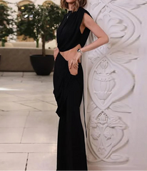 Woman in a black dress standing against a decorative white wall.