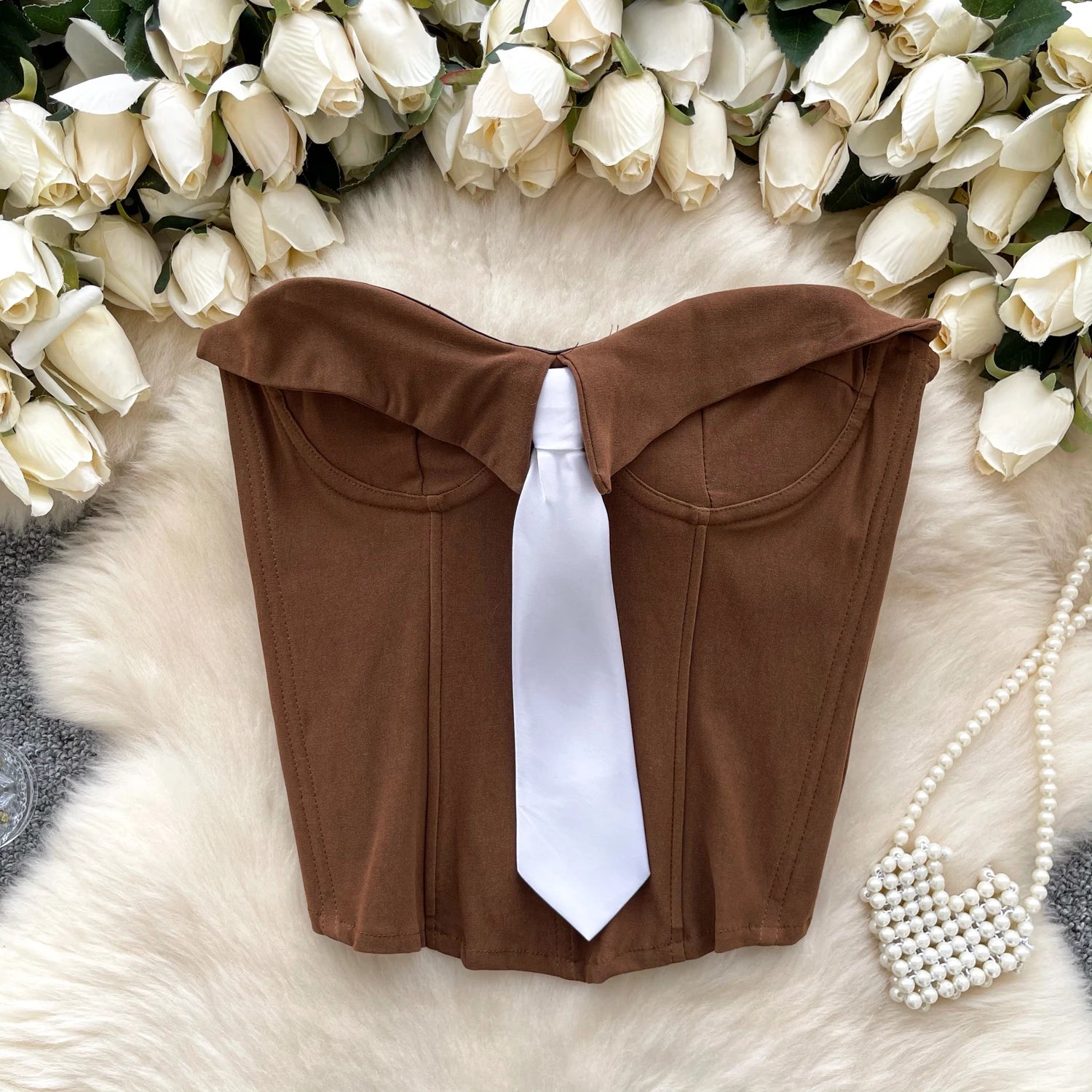 Brown top with a white tie on a fur surface surrounded by white roses.