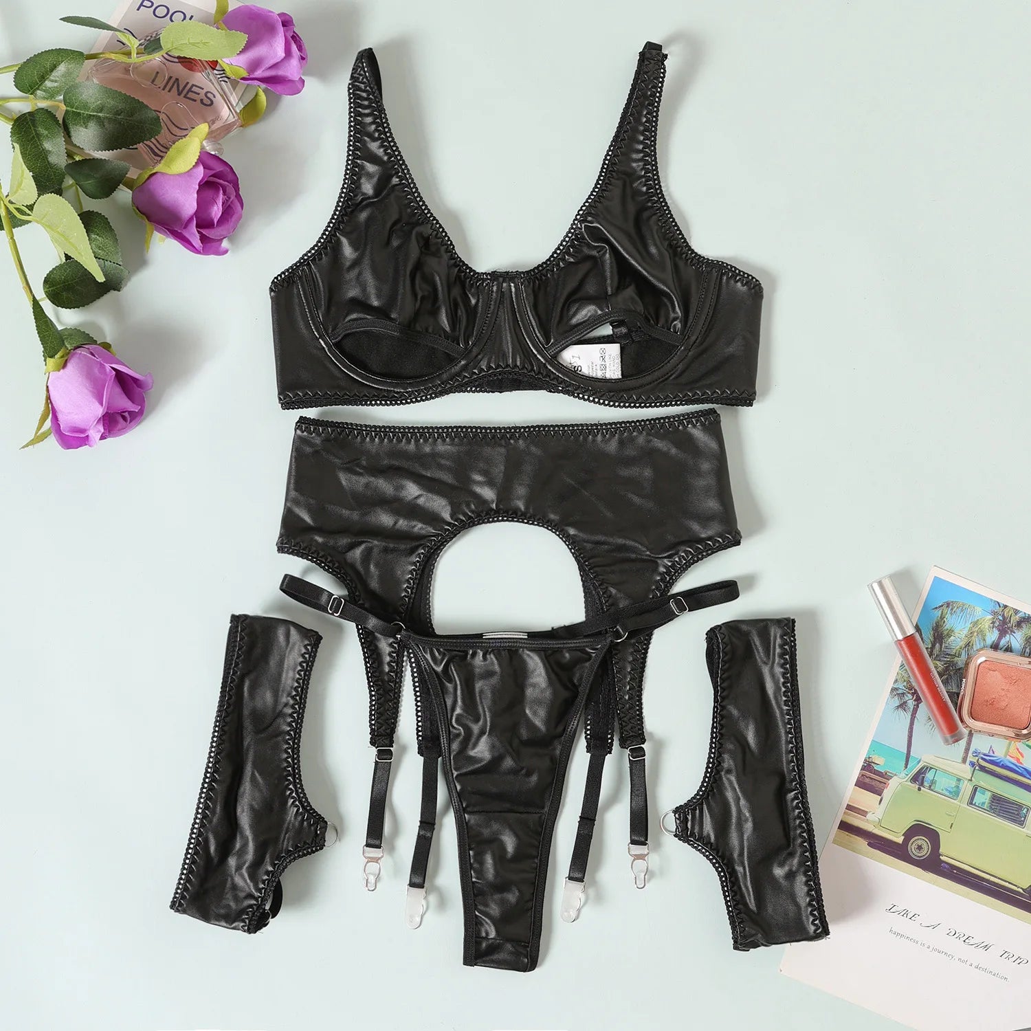 Black lingerie set with garters on a light surface with flowers and a magazine.