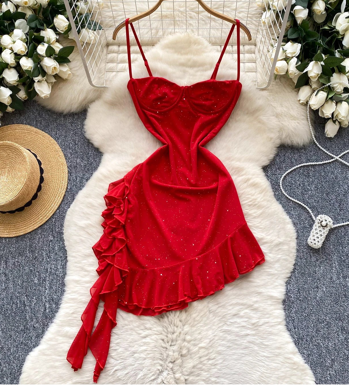 Red dress with ruffles on a white fur rug surrounded by flowers and a hat.