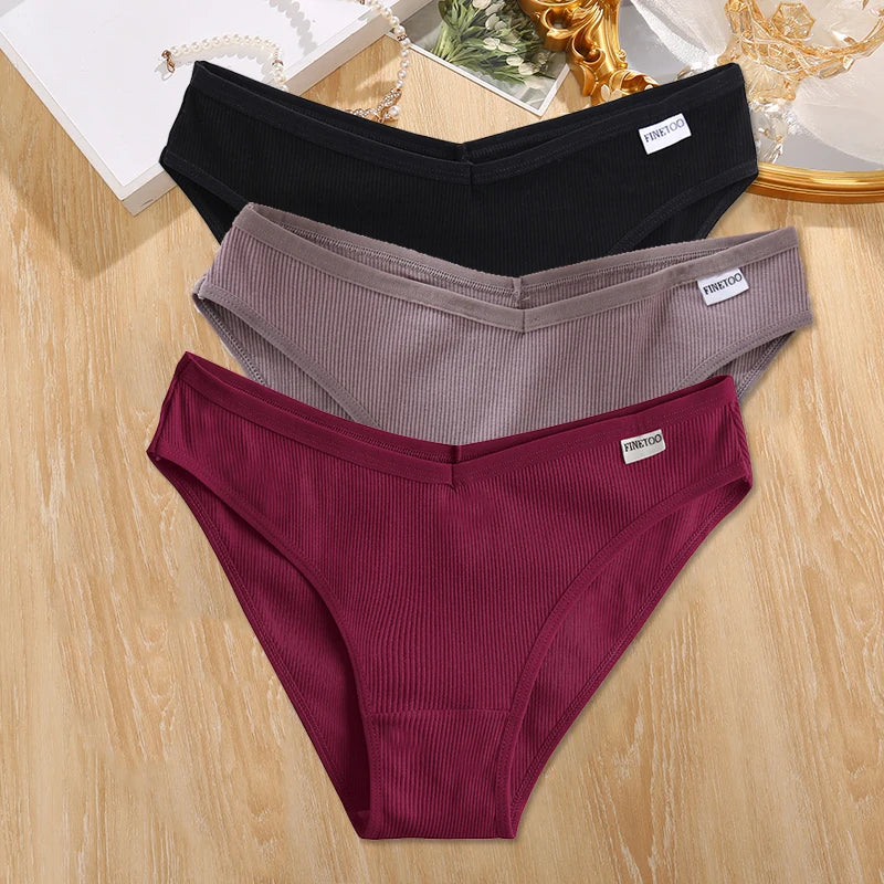 Three pairs of ribbed underwear in black, gray, and burgundy on a wooden surface.
