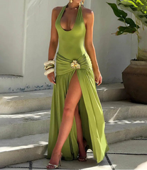 Woman in a green evening gown standing on stone steps with a white wall and plant in the background.
