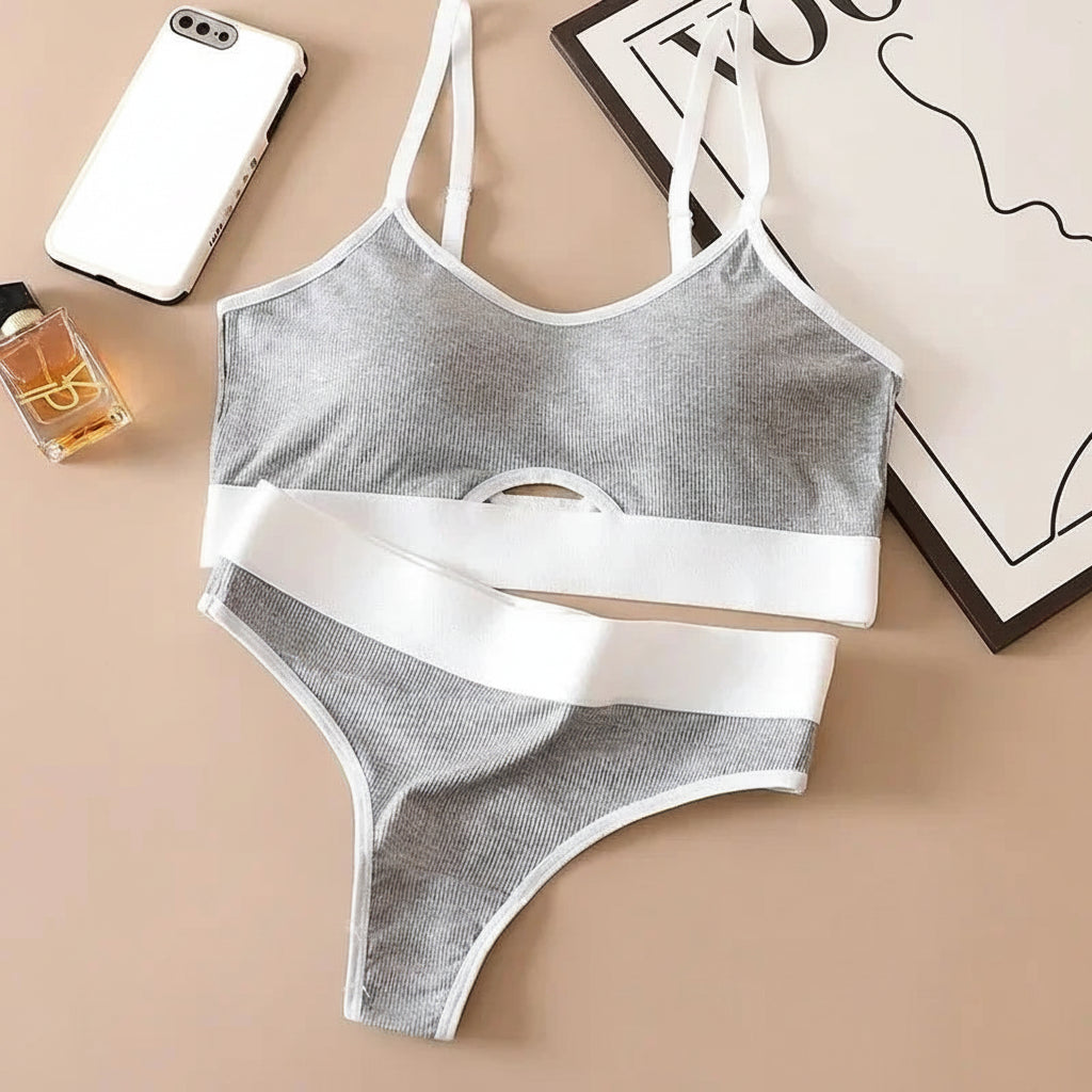 Gray and white bra and panties set on a beige surface with a phone and perfume bottle.