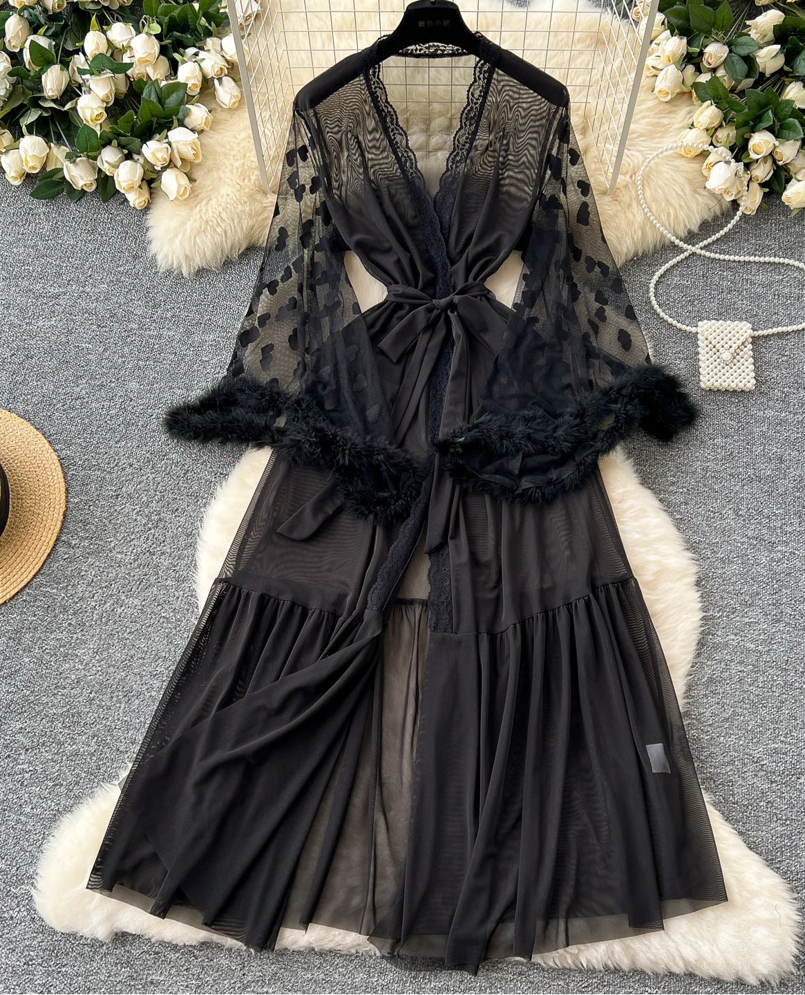 Black lace dress with feather details on a hanger against a floral and fur background
