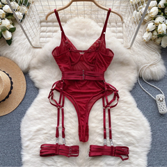Red lingerie set with garters on a white fur rug surrounded by flowers and a hat.