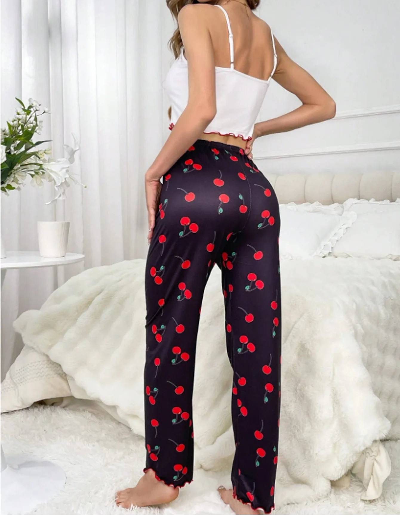 Woman wearing black pants with red cherry pattern in a bedroom setting