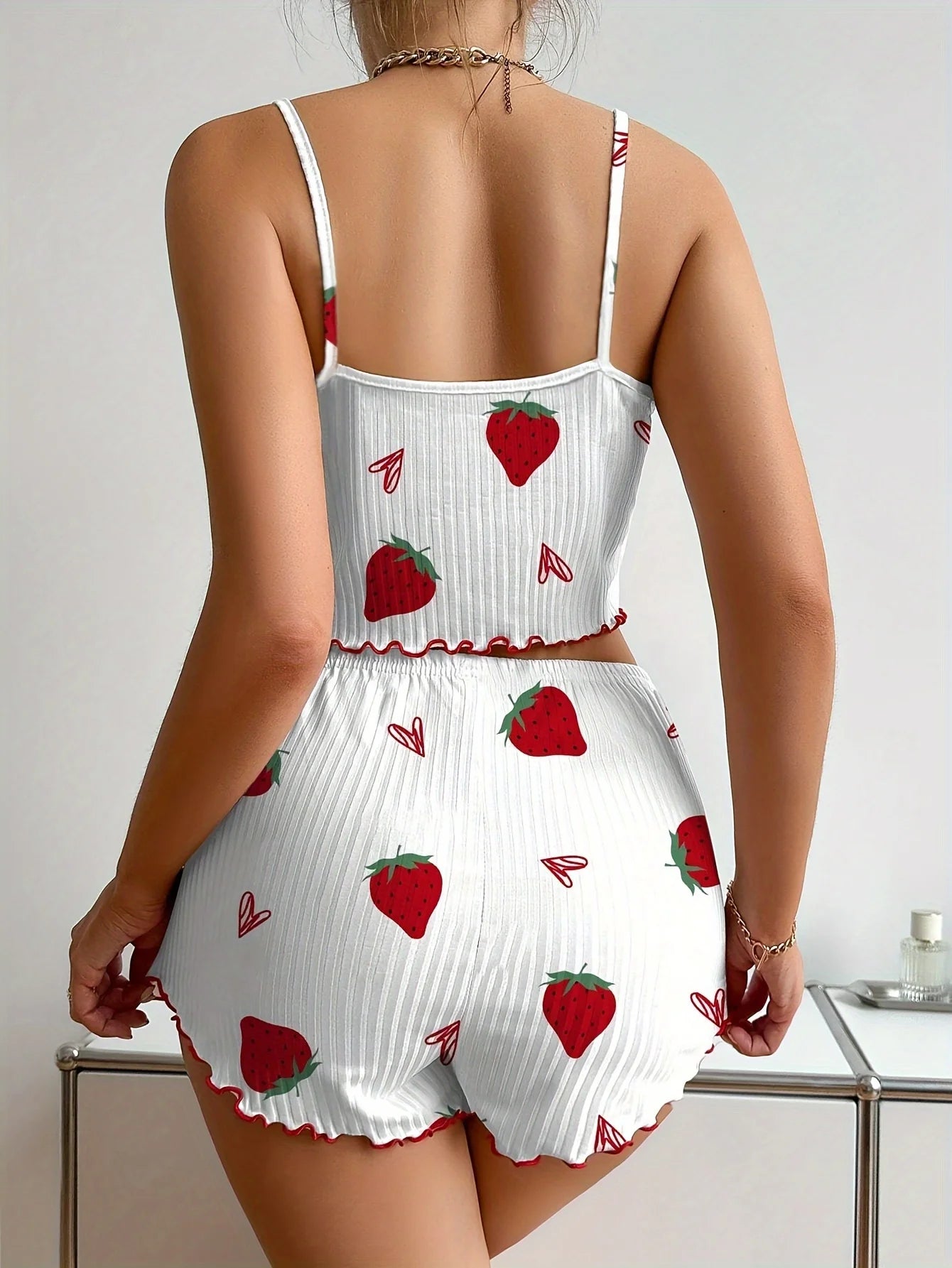White romper with red strawberry pattern worn by a person on a plain background