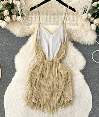Gold fringe dress on a hanger with a white textured surface and floral decorations.