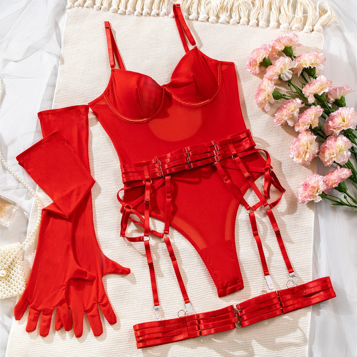 Red lingerie set with matching belt and gloves on a textured surface with flowers.