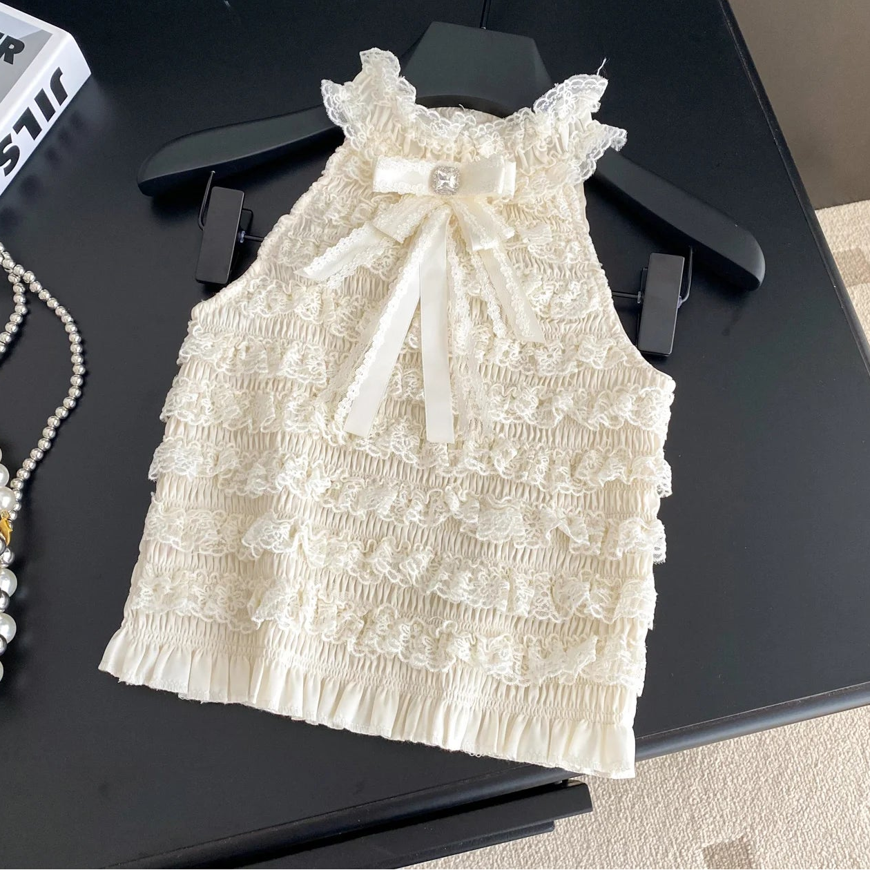 White lace dress with a bow on a black hanger against a dark surface.