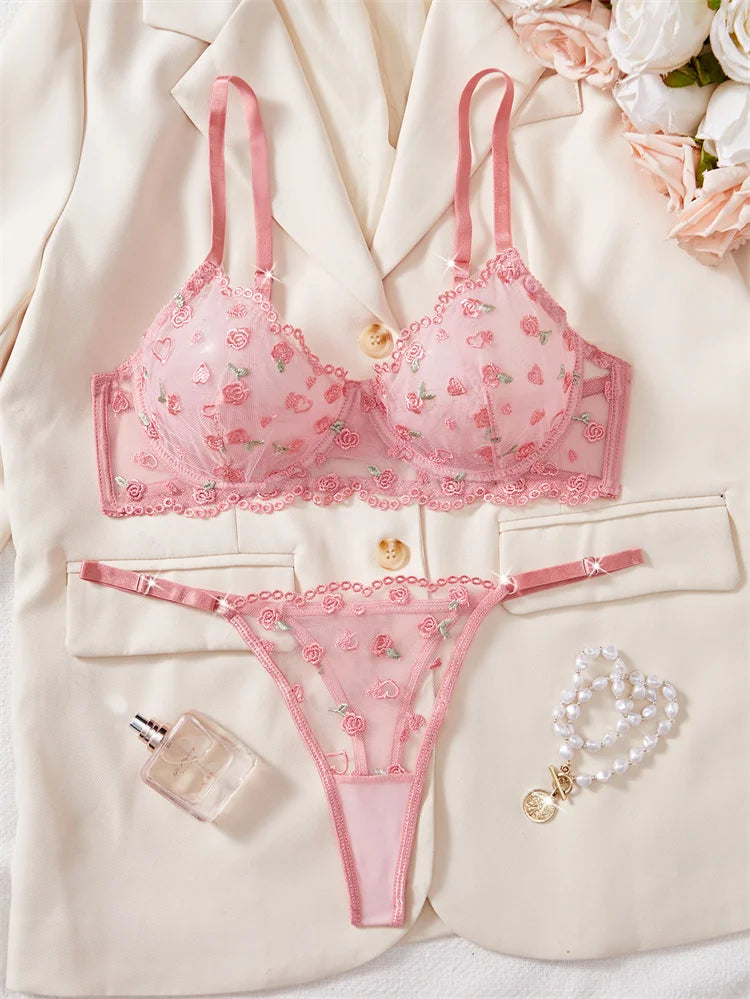 Pink floral lingerie set with a robe, perfume bottle, and bracelet on a light background