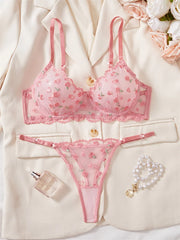 Pink floral lingerie set with a robe, perfume bottle, and bracelet on a light background